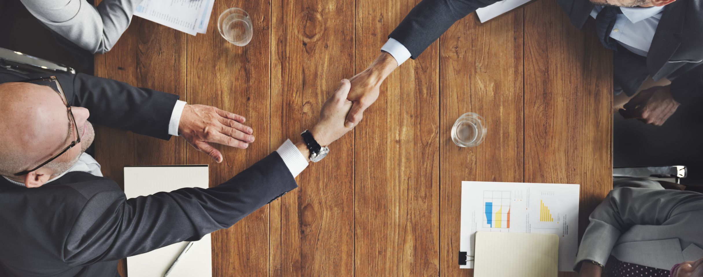 People around a table, 2 of them shaking hands